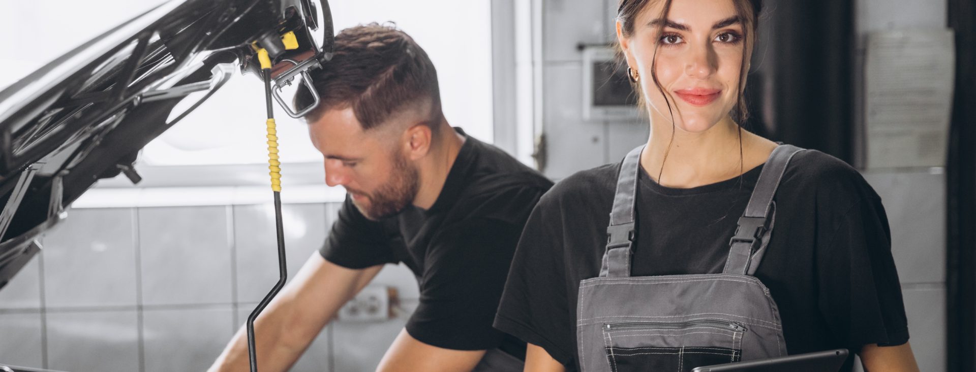 Auto service, repair, maintenance concept. Mechanic checks the car at the service station. Charming woman and bearded engineer use tablet check car battery