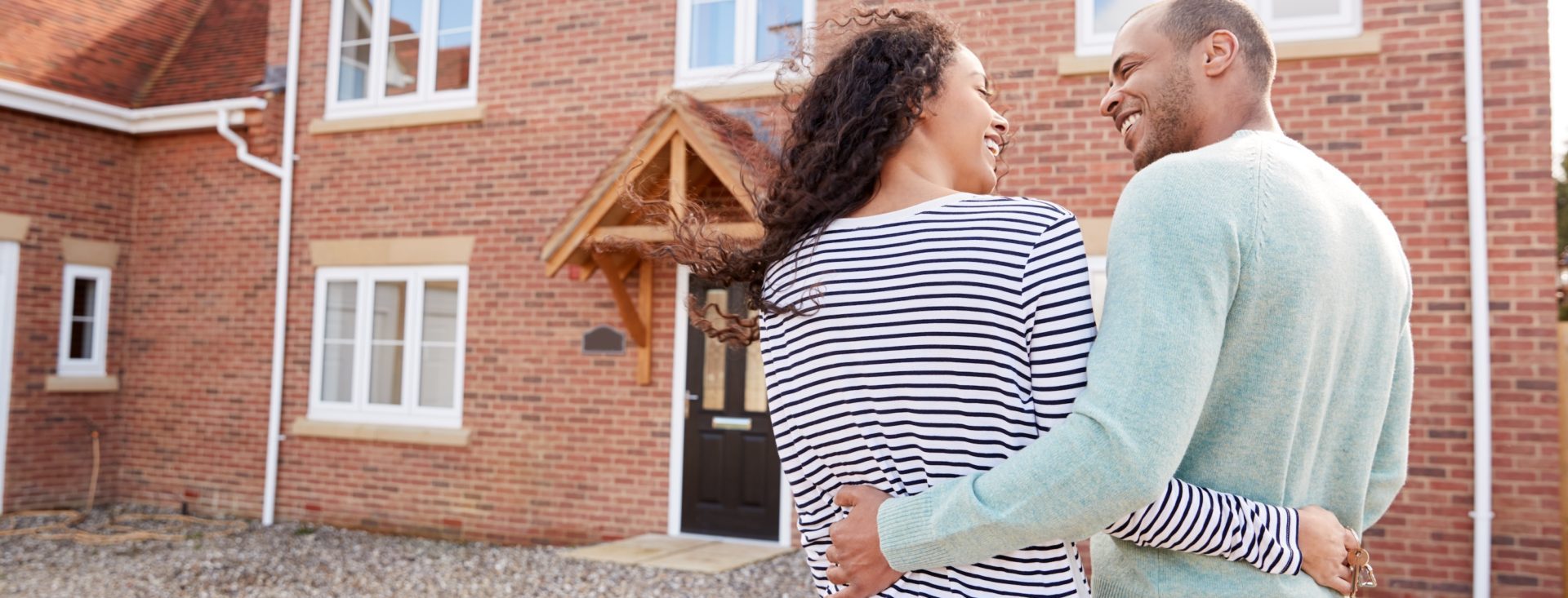 Rear View Of Couple Standing Outside New Home On Moving Day Looking At House