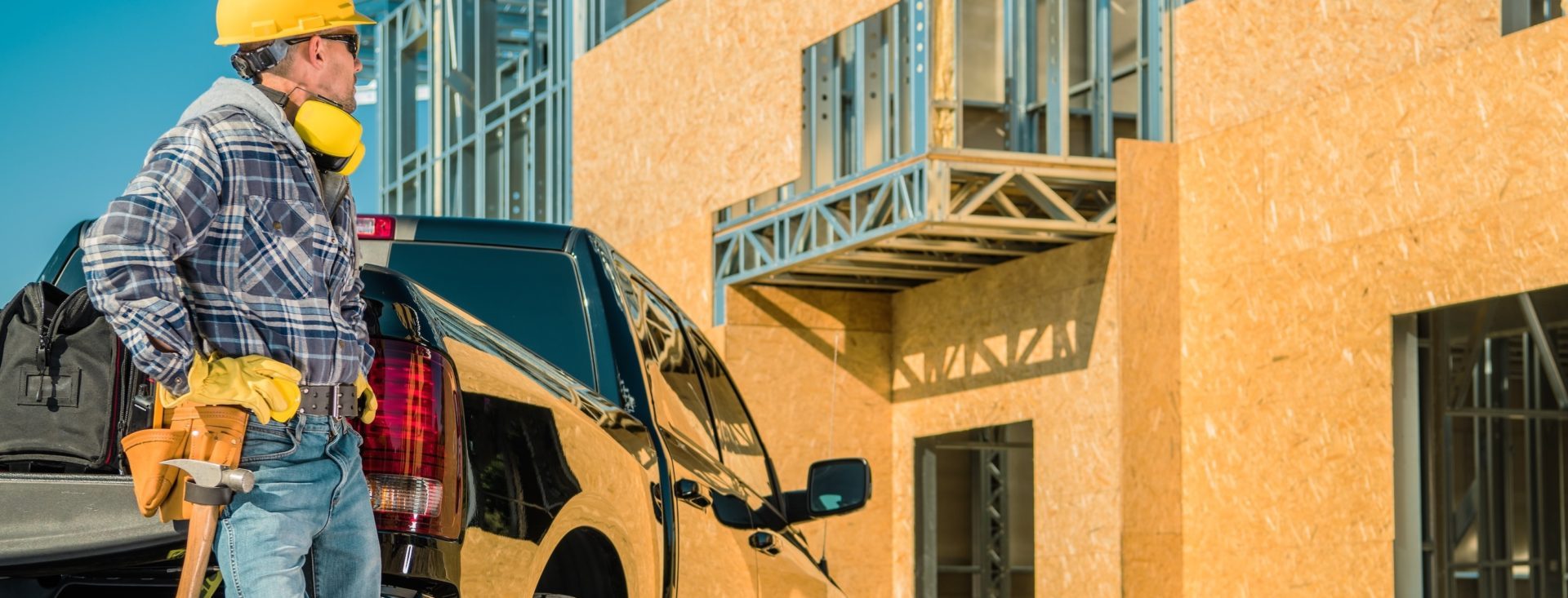 Residential Construction Site. Young Caucasian Contractor Worker in His 30s and His Pickup Truck in Front of Newly Constructed Building. Metal Frame and Plywood Walls. Residential Construction Site:construction site,contractor,pickup,work,job,labor,vehicle,car,truck,business,industry,industrial,residential,metal,frame,manager,hard hat,caucasian,investment,market,real estate,development,heavy duty,horizontal
