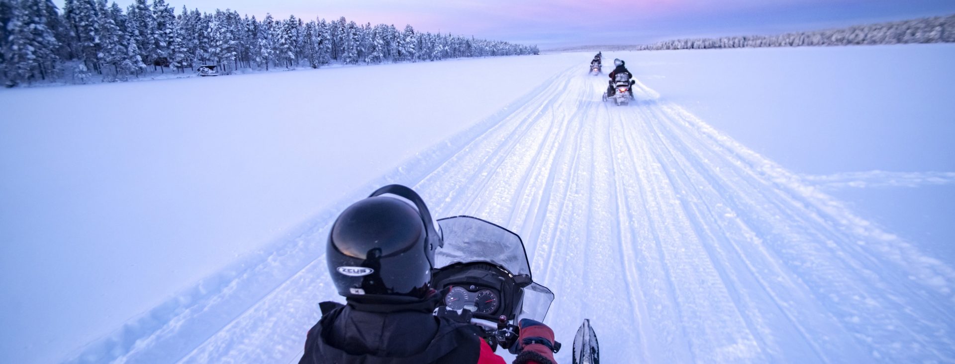 Snowmobiling on the frozen lake at sunset at Torassieppi, Lapland, Finland