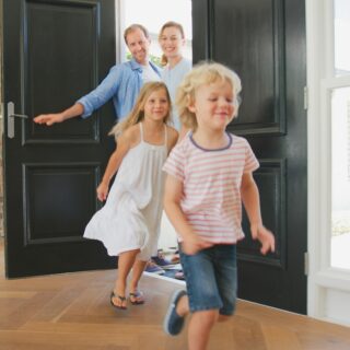 Family Returning Home With Excited Children Running Ahead Through Front Door
