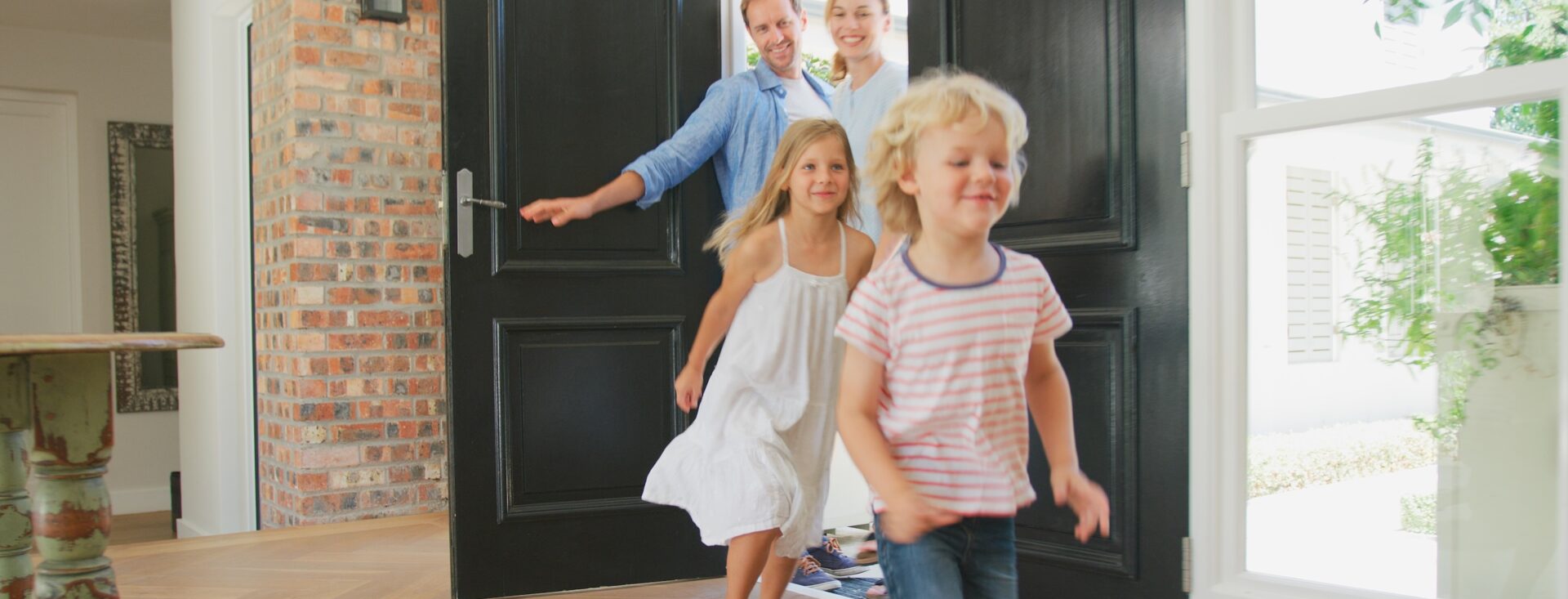 Family Returning Home With Excited Children Running Ahead Through Front Door